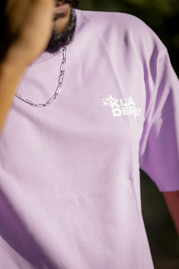 Close-up of a man wearing a pastel lavender Kläder unisex oversized t-shirt with a white logo print on the chest.