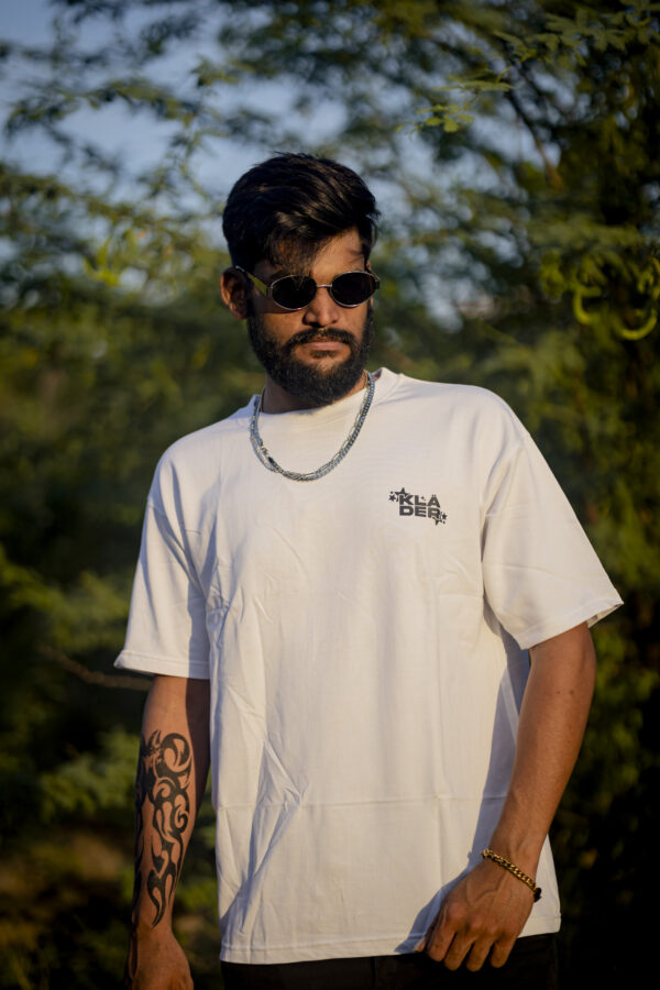 Man wearing a white T-shirt with a small klader logo on the chest, standing outdoors with sunglasses and accessories