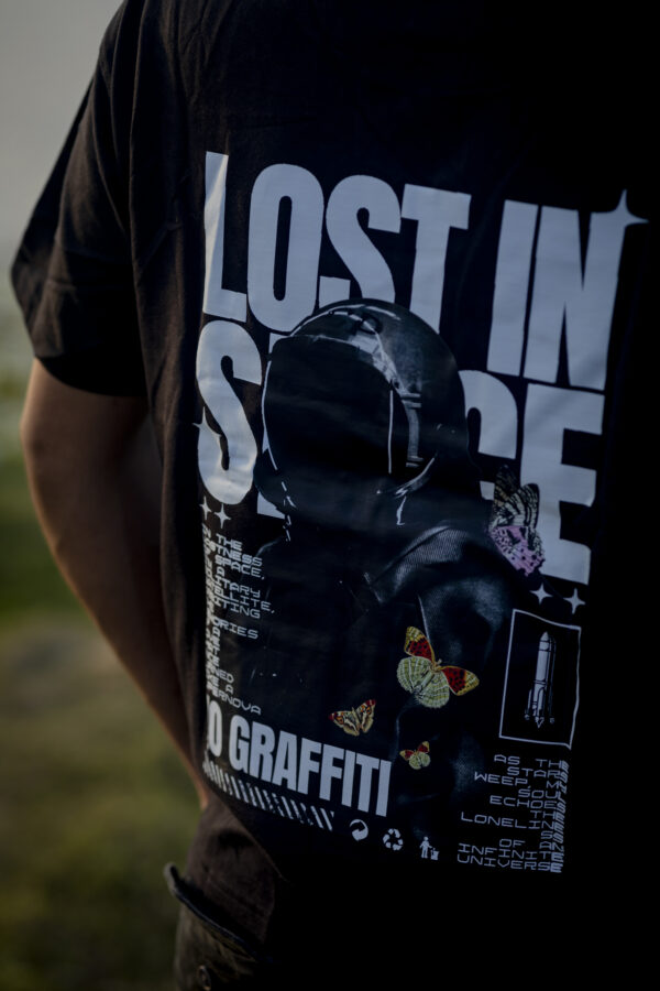 Back view of black oversized t-shirt with astronaut graphic and "Lost in Space" text design, worn outdoors