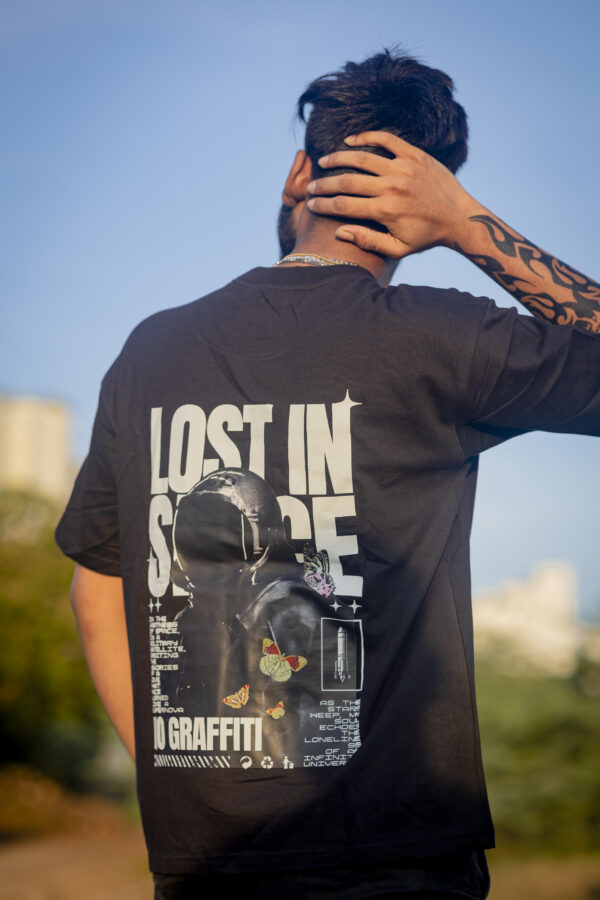 Person wearing black oversized t-shirt with astronaut and "Lost in Space" graphic design outdoors under blue sky.