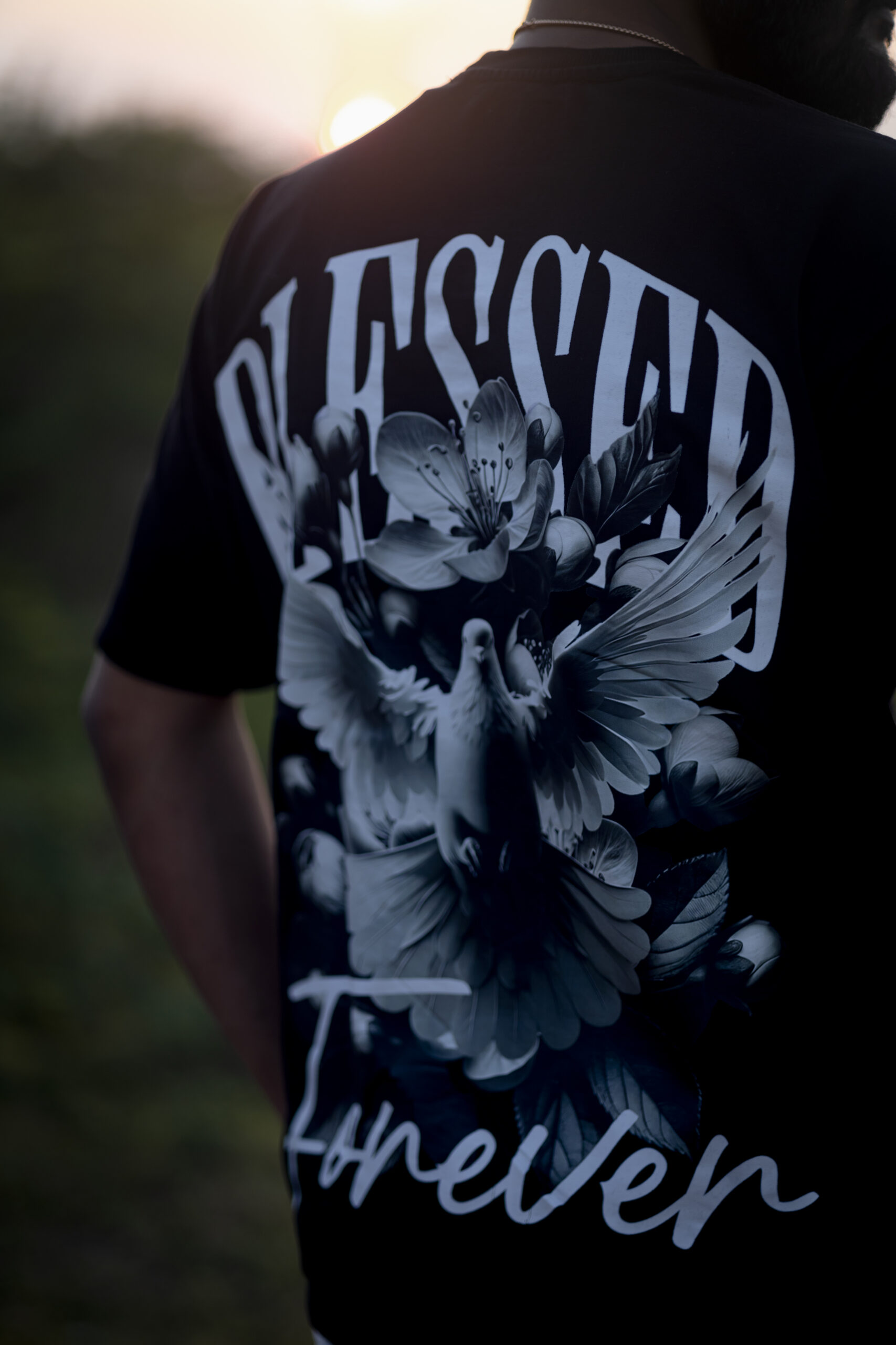 Back view of a black oversized t-shirt with white floral artwork, dove illustration, and the words “Blessed Forever.”